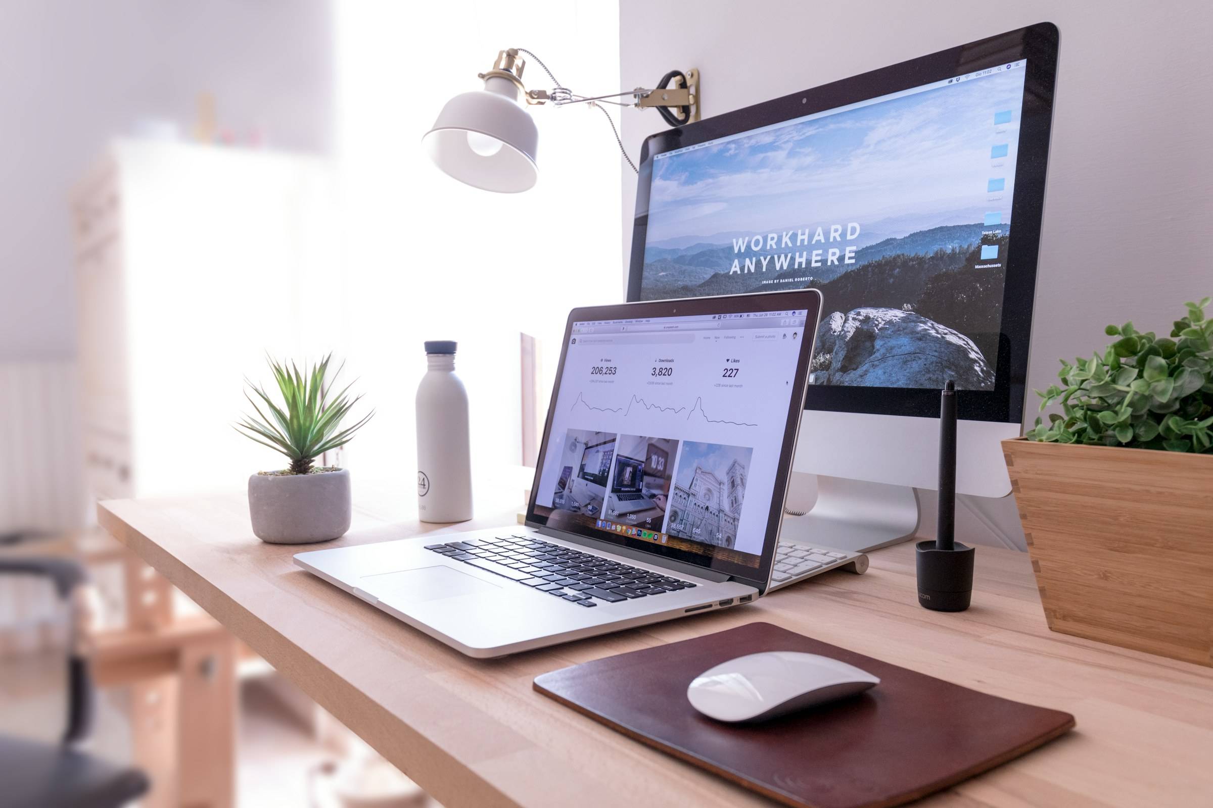 Heller Arbeitsplatz mit Laptop und großem Monitor, auf dem eine Website geöffnet ist
