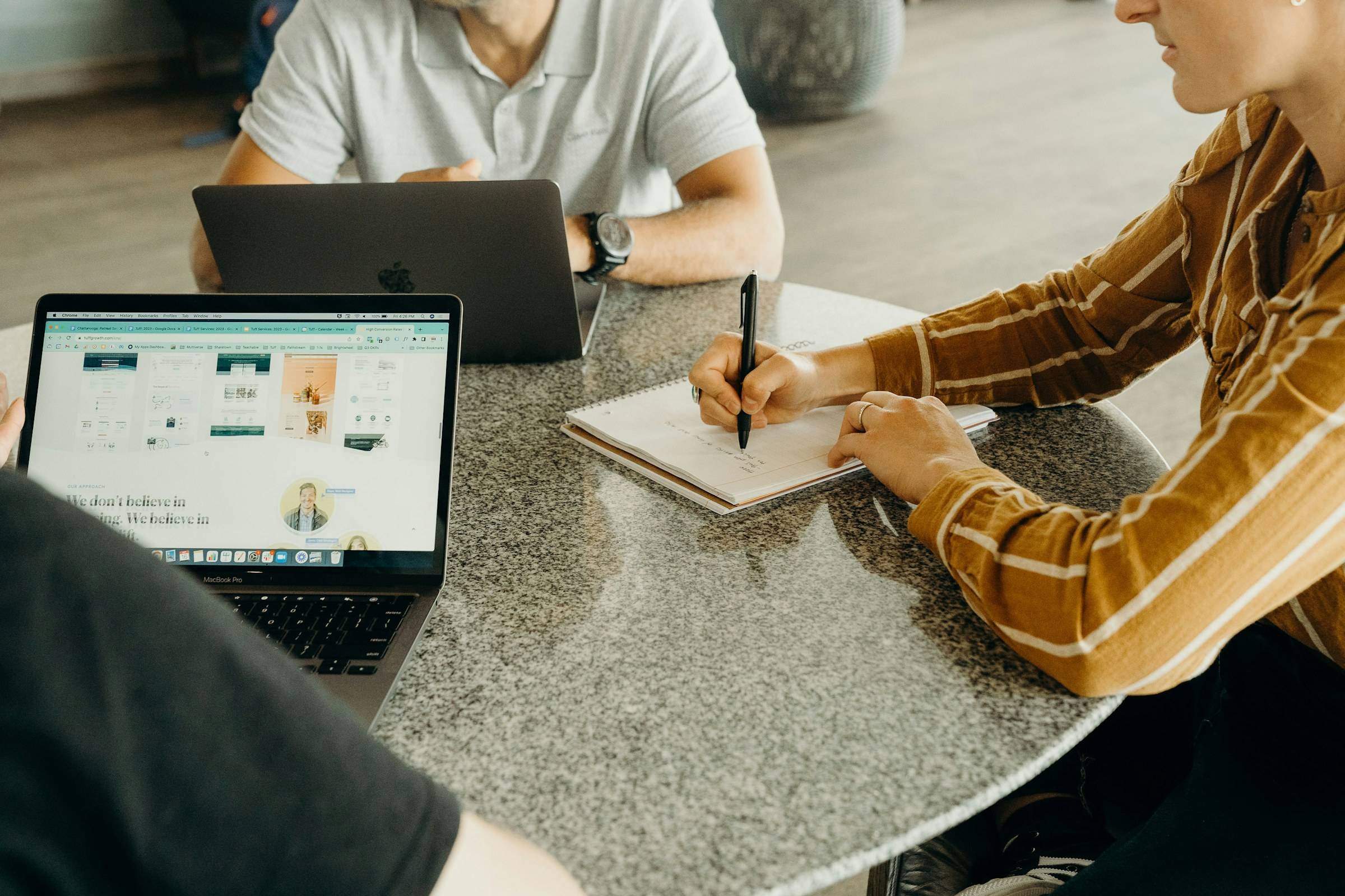 Drei Personen besprechen sich an einem runden Tisch mit Laptops und Notizbüchern
