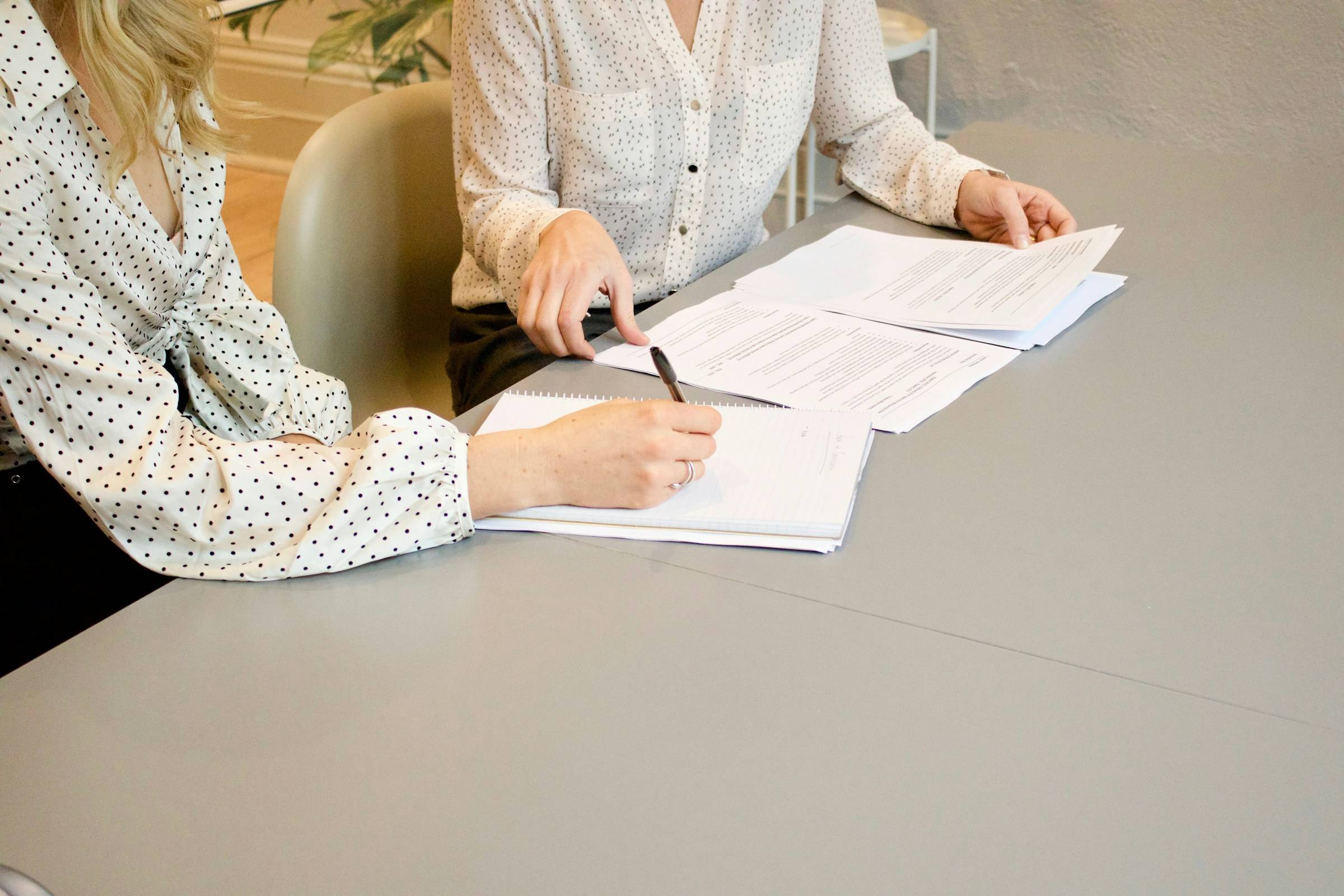 Zwei Personen am Tisch, eine unterschreibt ein Dokument, daneben weitere Unterlagen